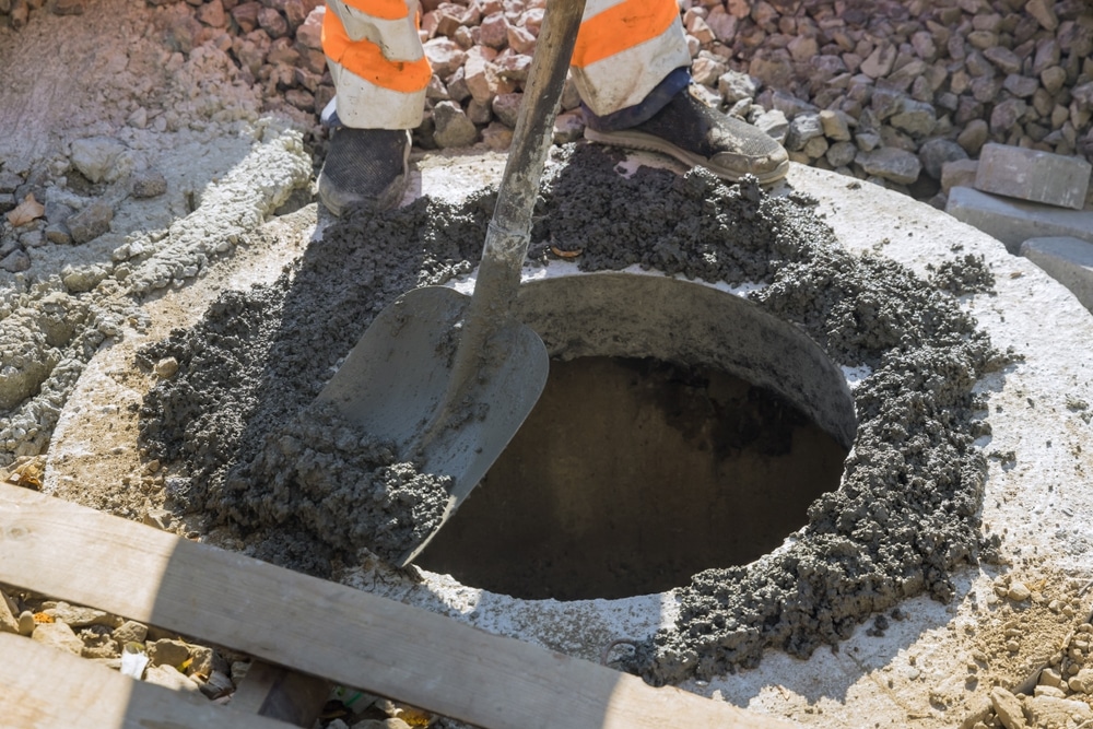 Bétonnage et scellement d'un regard de visite circulaire Ouvrier étalant du béton frais à la pelle autour d'un regard de visite circulaire sur un chantier de construction.