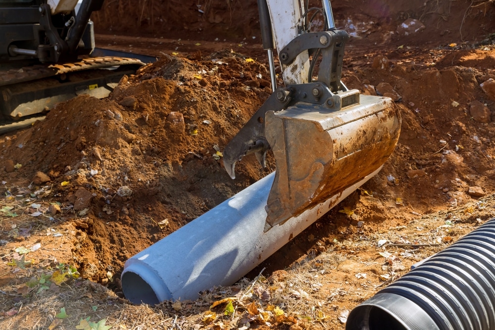 Installation de canalisation béton avec une excavatrice Excavatrice plaçant une buse en béton dans une tranchée pour des travaux de drainage et d'assainissement.