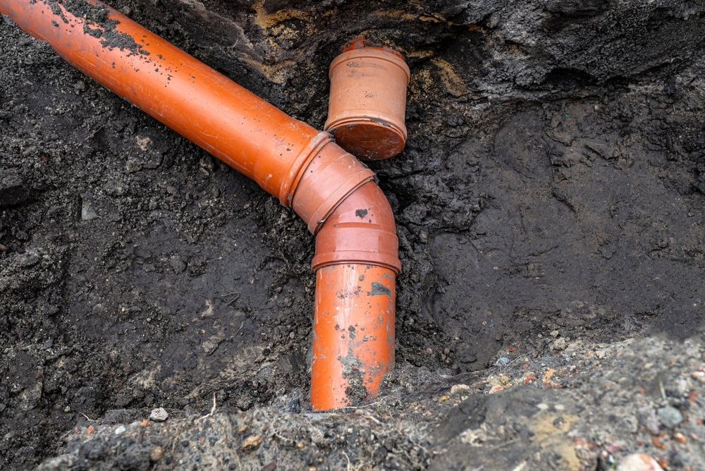 Installation de canalisation en PVC orange pour l'évacuation des eaux usées dans une tranchée creusée.