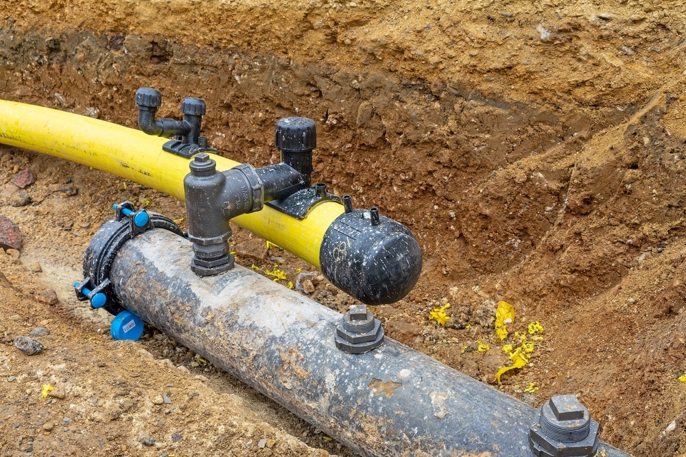 Installation de tuyaux de gaz et d'eau en tranchée Tuyaux de gaz jaune et conduite d'eau grise dans une tranchée d'excavation avec raccords et vannes.